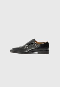 Sorte lærmonkstrap-sko med spiss tå, enkelt spenne, glatt tekstur og flat hæl. Minimalistisk design med diskret merking.