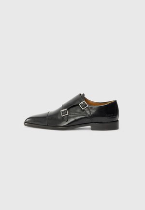 Sorte lærmonkstrap-sko med spiss tå, enkelt spenne, glatt tekstur og flat hæl. Minimalistisk design med diskret merking.
