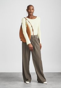 Svetlozelený prúžkovaný top s dlhým rukávom a gombíkovými detailmi, kombinovaný so sivými širokými nohavicami a hnedou kabelkou cez rameno. Biele špicaté topánky.