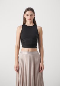 Top corto negro sin mangas con escote redondo y detalle de fruncido, combinado con una falda larga plisada de un tono beige claro con una cinturilla de satén.