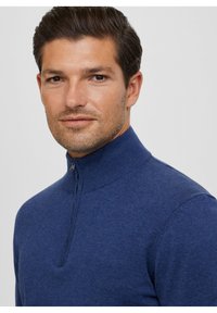 Maglione blu con zip, colletto alto, realizzato in morbido tessuto a maglia testurizzato, caratterizzato da una piccola zip metallica e un design aderente.
