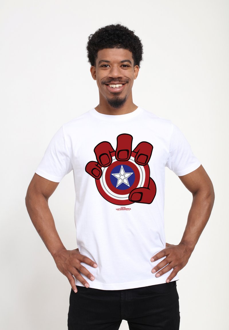 Hvid bomulds t-shirt med et grafisk tryk af en rødhandsket hånd, der griber fat om et cirkulært skjold med røde, blå og hvide farver og et stjernedesign.