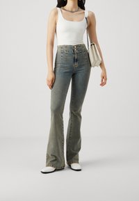 Utsvängda jeans i ljusblå denim med hög midja, tillsammans med en åtsittande vit tanktop och en liten vit handväska. Silverhalsband.