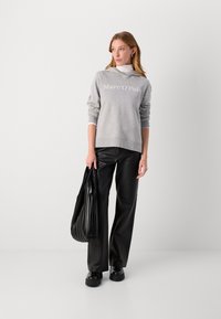 Hellgrauer Sweatshirt mit dem Aufdruck "Marc O'Polo", kombiniert mit schwarzen, weiten Lederhosen und einer schwarzen, gefalteten Tragetasche. Flache schwarze Schuhe.