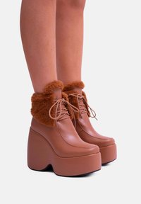 Stivali platform marroni in morbida ecopelle con un polsino di pelliccia soffice, punta rotonda, chiusura con lacci e un design con tacco spesso.
