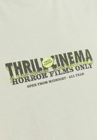 Hvid bomulds T-shirt med sort og stærkt grøn grafiktekst: "THRILL CINEMA," "KUN HORRORFILM," og "ÅBEN FRA MIDNAT - HELE ÅRET."