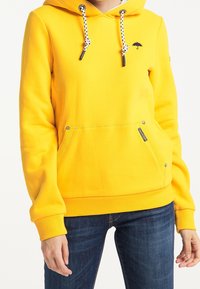 Sweat à capuche en coton jaune avec une poche avant, des cordons de serrage contrastants et un petit détail de logo. Texture douillette, poignets et ourlet côtelés.