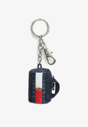 Metalowy brelok do kluczy z łańcuszkiem i klipsem przypiętym do małej granatowej saszetki z logo Tommy Jeans i pionowymi czerwono-biało-niebieskimi paskami.