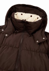 Tmavohnedá prešívaná bunda s vysokým golierom, striebornými patentkami a zipsom. Vnútorná podšívka je z krémovej látky s hnedými bodkami.