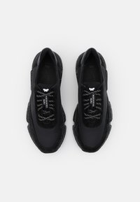 Paar zwarte chunky sneakers met patroonveters, vlindermotief op de tong en een gespikkelde dikke zool, gezien van boven op een witte achtergrond.