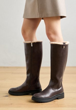 Braune knielange Stiefel mit einer glatten Lederoberfläche, gefälschtem Pelzbesatz an der Oberseite, seitlichem Reißverschluss und stabiler strukturierter Gummisohle.