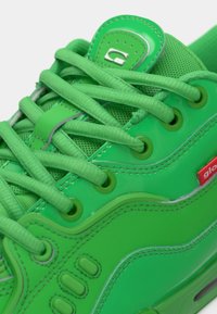 Baskets vert vif avec lacets assortis, matériaux en mesh et cuir, œillets métalliques et une petite étiquette de marque rouge sur le côté.
