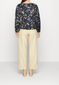 Blusa floreale a maniche lunghe nera con motivi colorati. Abbinata a pantaloni cream a gamba larga e scarpe con tacco blocco beige.