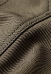 Tessuto marrone, testurizzato, con un sottile motivo a costine e cuciture visibili, che evidenzia pieghe e drappeggi nel materiale.
