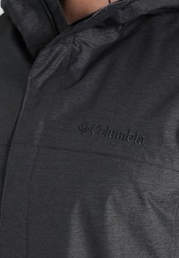 Giacca sintetica nera con cappuccio, superficie testurizzata e logo Columbia, dotata di chiusura con zip e cuciture a vista.