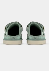 Πράσινα παπούτσια UGG με λείο εξωτερικό, μαλακή επένδυση, λουράκια στο πίσω μέρος, υφή στη πλευρά και μπεζ λαστιχένια σόλα.