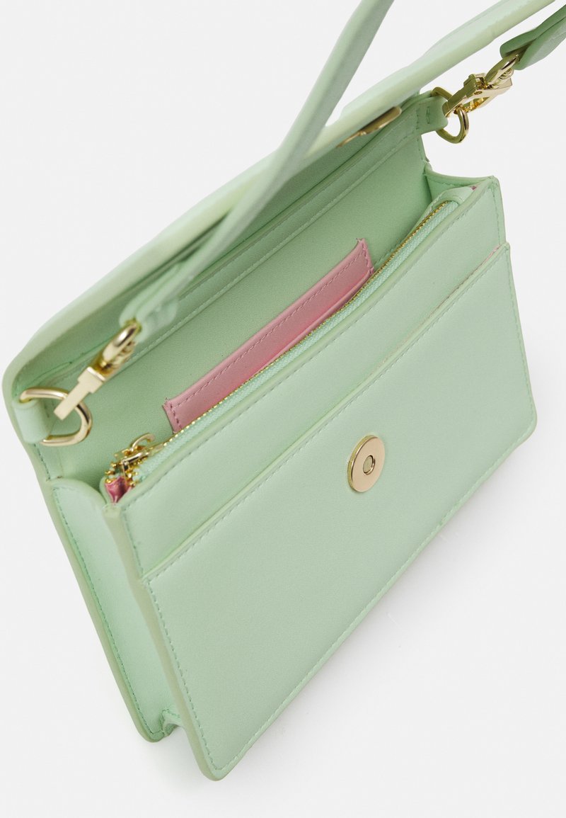 Helle grüne Handtasche, geöffnet, um das rosa innere Reißverschlussfach sowie die goldenen Verschluss- und Riemenbefestigungen zu zeigen.