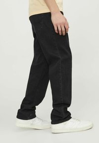 Svarta raka jeans med synlig sömnad, sidofickor och en lätt slitdagsyta, i kombination med vita sneakers.