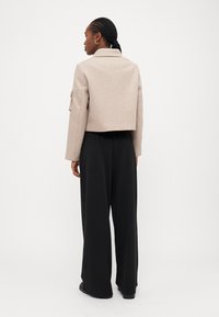 Beige kort jacka i mjuk ullblandning, vida ärmar med knyt, kombinerad med lösa svarta byxor. Slät textur, enkel design.