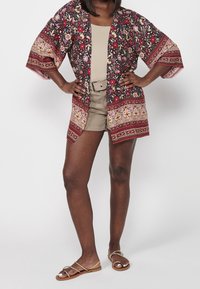 Lichtgewicht bloemige kimono in marineblauw en bordeauxrood, met wijd uitlopende mouwen en een gegarneerde zoom. Gecombineerd met een beige tanktop en shorts.