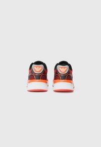 Black and red athletic shoes with white soles, featuring a textured mesh upper and an angular logo on the heel.
