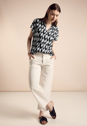 Zwart-wit gestreept kortemouwen shirt gecombineerd met losse beige broek en zwarte instapsandalen op een neutrale achtergrond.