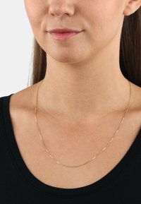Złota łańcuszek naszyjnik z gładką, wypolerowaną powierzchnią; drobne ogniwa tworzą delikatny, minimalistyczny wzór. Noszony na szyi.