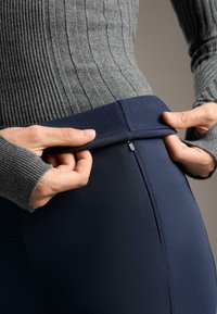 Tengerészkék leggings sima, rugalmas anyagból, magas derékrésszel, diszkrét cipzárral és szürke bordázott hosszú ujjú felső részlettel.