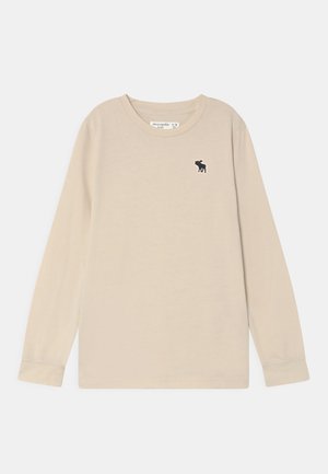 Beige Langarmshirt mit Rundhalsausschnitt für Kinder, mit kleinem schwarzem Elch-Logo auf der linken Brust und gerippten Bündchen.
