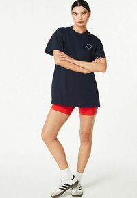 Tricou bleumarin cu mâneci scurte și guler rotund, asortat cu pantaloni scurți roșii pentru ciclism, sosete albe și adidași alb-negru.