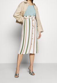 Randig midikjol i vitt, grönt och orange, med knut vid midjan, framknappar, kombinerad med en ljusblå topp och beige jacka.