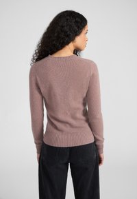 Suéter de punto rosa claro, con mangas largas y puños y dobladillo acanalados. Textura suave, escote redondo, visto desde la parte de atrás.