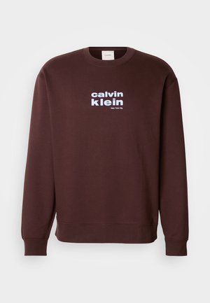 Brun crew neck sweatshirt lavet af bomuld, med et hvidt logo "calvin klein" og "New York City" trykt på forsiden i fede typer.
