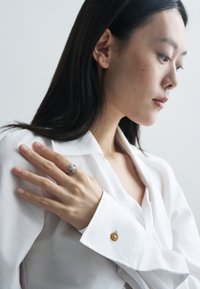 Ezüst gyűrű bonyolult mintával, amely egy kézen viselve, tiszta fehér inggel párosítva, amelyen arany gomb díszítés található az ingujjon.