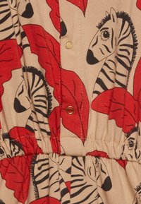 Wielokolorowa tkanina sukienkowa z beżowym tłem, ozdobiona czerwonymi wzorami liści oraz motywami zebry w czerni i bieli, podkreślona złotymi guzikami.