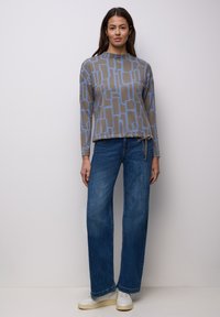 Top de manga larga con estampado en tonos grises y azules, cuello redondo y detalle de cordón, combinado con vaqueros de pierna ancha azules y zapatillas blancas.