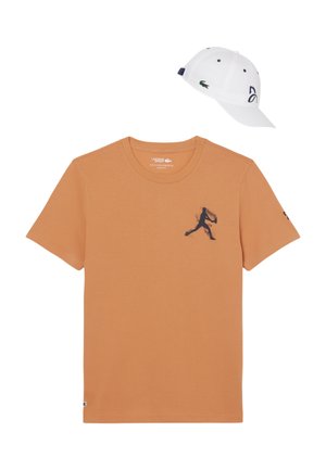 Camiseta de manga corta color tan con silueta azul marino de un jugador de tenis en el pecho y gorra blanca de béisbol con logotipo azul marino y emblema verde de cocodrilo.