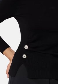 Maglione nero a costine con uno spacco laterale e due bottoni decorativi in tono argento. Tessuto liscio con maniche lunghe aderenti.