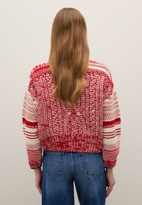 Maglione a maglia con motivo rosso e crema, vestibilità ampia, orlo a costine e maniche lunghe, abbinato a jeans blu.