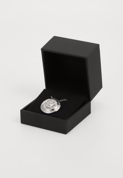 Pandantiv din argint cu motive complicate, așezat într-o cutie de bijuterii neagră. Dispune de un sistem de prindere cu lanț și un design circular cu detalii ornate.