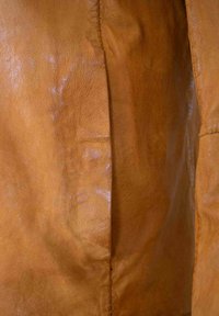 Garderobe aus braunem Leder mit sichtbarer Textur und Glanz, die eine Nahtdetails entlang der Kante aufweist. Glatte und geschmeidige Oberfläche.