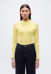 Κίτρινο πουλόβερ με ριγέ υφή, εφαρμοστό σχέδιο και ψηλό λαιμό, σε συνδυασμό με σκούρο μπλε τζιν παντελόνι με αντίθετη ραφή και εμπρόσθιες τσέπες.