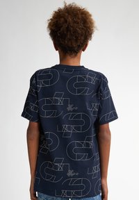 Camiseta de algodón azul marino con un patrón de líneas geométricas blancas, mangas cortas y cuello redondo. Se muestra la vista posterior.
