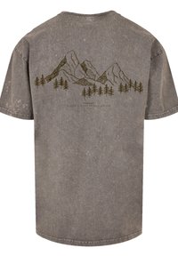 Graues Baumwoll-T-Shirt mit lockerer Passform, auf der Rückseite mit einem Design von Bergen und Wald in Dunkelbraun. Der Stoff hat eine abgenutzte Textur.