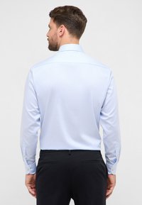 Chemise homme à manches longues, bleu clair avec de fines rayures verticales, poignets à boutons et col classique, en tissu lisse.
