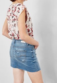 Květinová halenka s krátkými rukávy v krémové barvě, spárovaná s modrou denimovou minisukní s třepeným lemem a dvěma zadními kapsami.