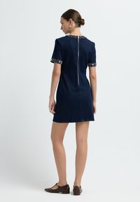 Robe en denim avec une silhouette adaptée, de couleur bleu foncé, à manches courtes et avec des accents à pois aux poignets et au col, dotée d'une fermeture éclair au dos.