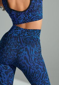 Športni top in legice z modrim leopardjim vzorcem, ki vključujejo teksturirano tkanino, visok pas in izrezane detajle na vrhu.