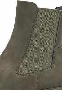 Bottine couleur olive en cuir suédé lisse avec des panneaux élastiques côtelés, ornée de coutures contrastées sur les côtés.
