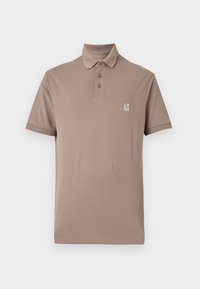 Hnedá polo tričko vyrobené z hladkej bavlny. Má golier, zapínanie na tri gombíky a malé biele logo na ľavom prsníku. Krátke rukávy.